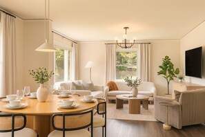 Uma sala de estar moderna com área de jantar, sofás, mesa de centro e televisão.