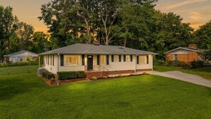 Une maison de plain-pied avec un porche à l’avant, des fondations en briques et une pelouse bien entretenue.