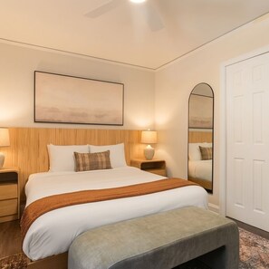 Une chambre d’hôtel avec un lit, des lampes de chevet, un miroir et un ventilateur de plafond.