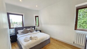 A bedroom with a large bed, two bedside tables, a window, and a radiator. - City Retreat in Central London (London)
