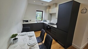 A modern kitchen with a skylight, dark cabinets, and a dining area set for four. - City Retreat in Central London (London)
