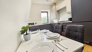 A modern dining area with a white table set for four, including plates, glasses, cutlery, and a potted plant. - City Retreat in Central London (London)
