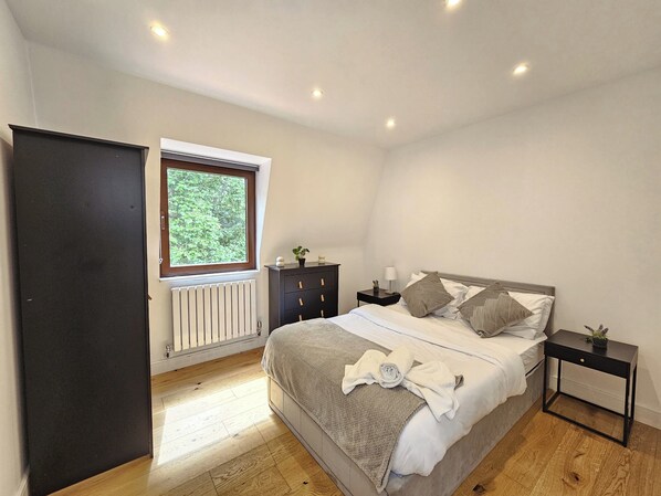 A bedroom with a bed, a nightstand, a dresser, a window, and a radiator.