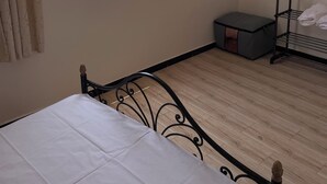 Un dormitorio con cama, una ventana con vista a la playa, un estante pequeño y un cojín.