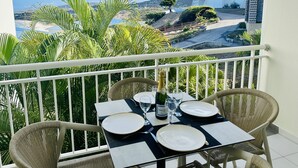 Un balcone con un tavolo apparecchiato per due persone, vista su una piscina e un paesaggio montuoso.