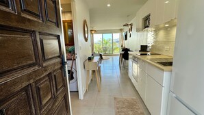Una cucina moderna con mobili bianchi, un'area pranzo con tavolo e sedie, e vista all'esterno tramite una porta scorrevole in vetro.