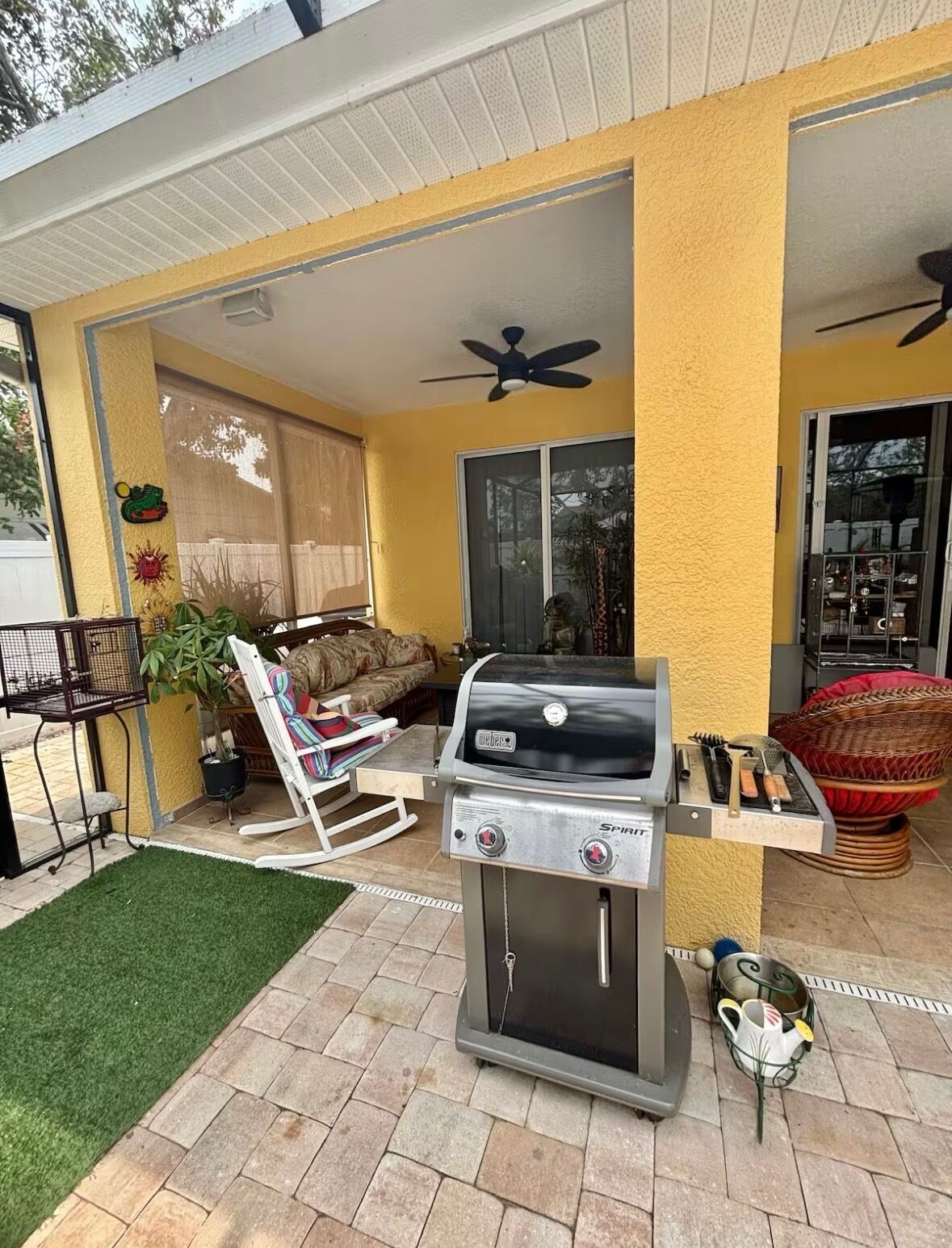 Een terras met een barbecue, een plafondventilator en een raam met uitzicht op een tuin.