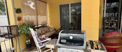 Een terras met een barbecue, een plafondventilator en een raam met uitzicht op een tuin.