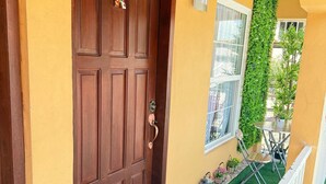 A wooden door with a colorful doormat, a small balcony with a table and chairs, and a green vertical garden. - Apartamento perfecto,  para viajes de trabajo o escapadas familiares. (San Pedro sula)