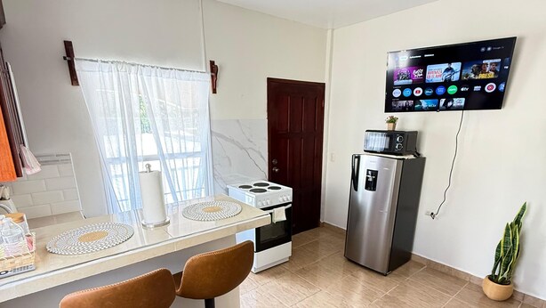 A modern kitchen with a built-in oven, a refrigerator, and a TV mounted on the wall displaying various channels. - Apartamento perfecto,  para viajes de trabajo o escapadas familiares. (San Pedro sula)