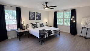 Ein Schlafzimmer mit einem Bett, zwei Nachttischen, einem Deckenventilator und zwei mit Vorhängen versehenen Fenstern.