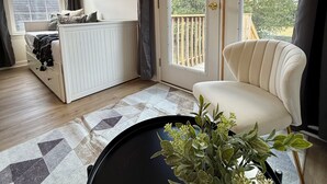 Ein modernes Wohnzimmer mit Sofa, Essbereich mit weißem Schrank, großem Fenster und Balkon mit Blick auf Bäume.