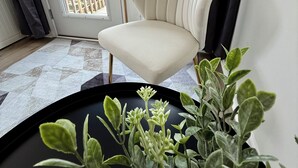 Ein Eckzimmer mit weißem Sessel, einem Blumentopf und Blick durch eine Glastür auf einen Balkon.