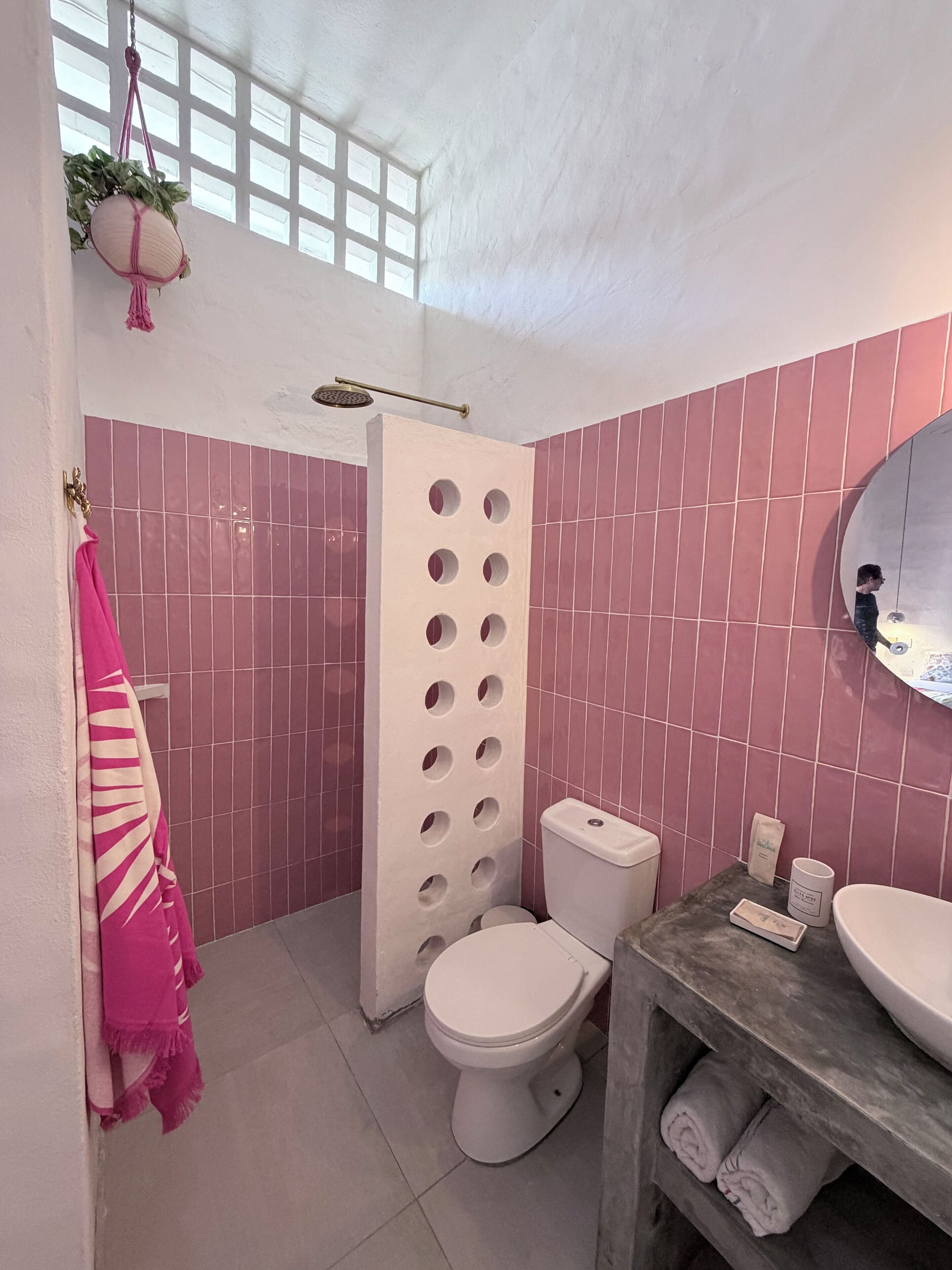 Une salle de bain avec des carreaux roses, des toilettes, un lavabo et un espace douche.