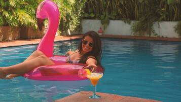 Una persona recostada en una piscina con un flotador de flamenco rosa y un cóctel al borde.