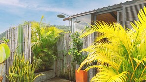 A garden with various tropical plants, a wooden fence, and a building with a metal roof. - Casa Amberes (Honda)
