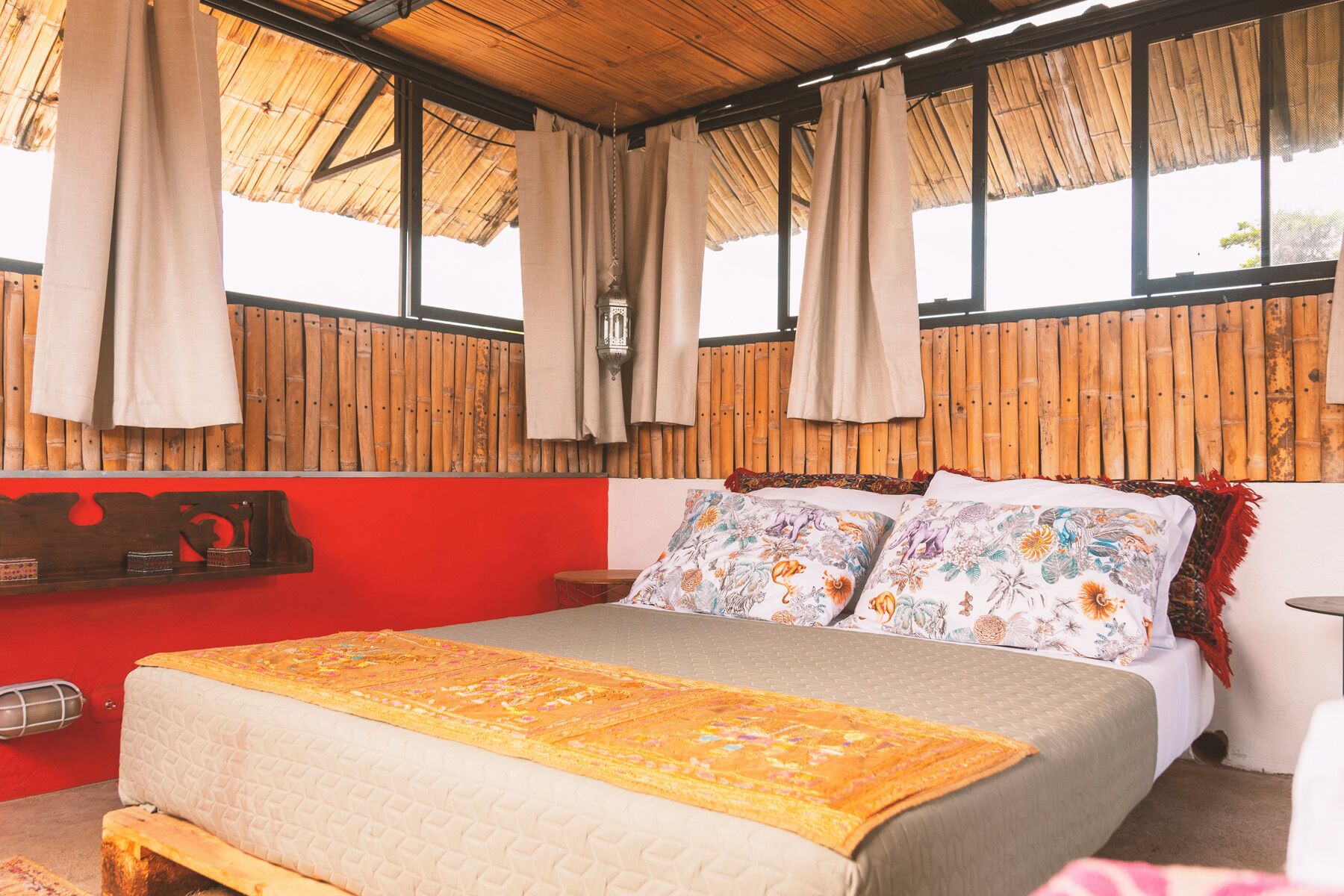Ein Zimmer mit einem Bett, einer roten Wand und einer Decke aus Bambus.