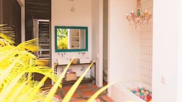 A bathroom with a white sink, a mirror with a green frame, a chandelier, and a bathtub filled with colorful balls.