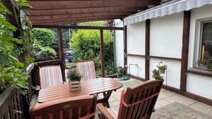 Un tavolo e delle sedie di legno sotto una pergola, con vista su un paesaggio verde e un’auto sullo sfondo.