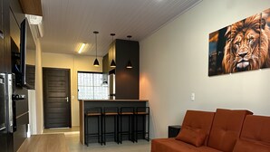 A modern living room with a sofa, a kitchen area with bar stools, and a dining table. - Your Sweet Home House in Içara near Criciúma!  A/C + bed with therapeutic massage+ (Içara)
