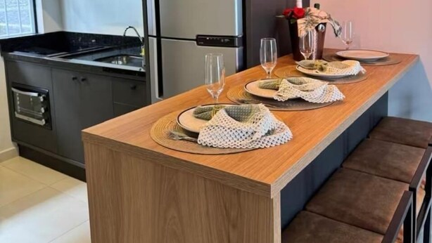 A modern kitchen with dark cabinetry, a central island with a wooden countertop, and pendant lighting. - Your Sweet Home House in Içara near Criciúma!  A/C + bed with therapeutic massage+ (Içara)