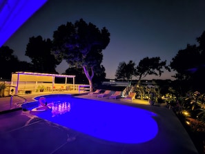 An outdoor swimming pool area with a covered seating area and lounge chairs.