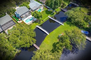 An aerial view of a property with a swimming pool, a dock, and a small bridge over a water body.