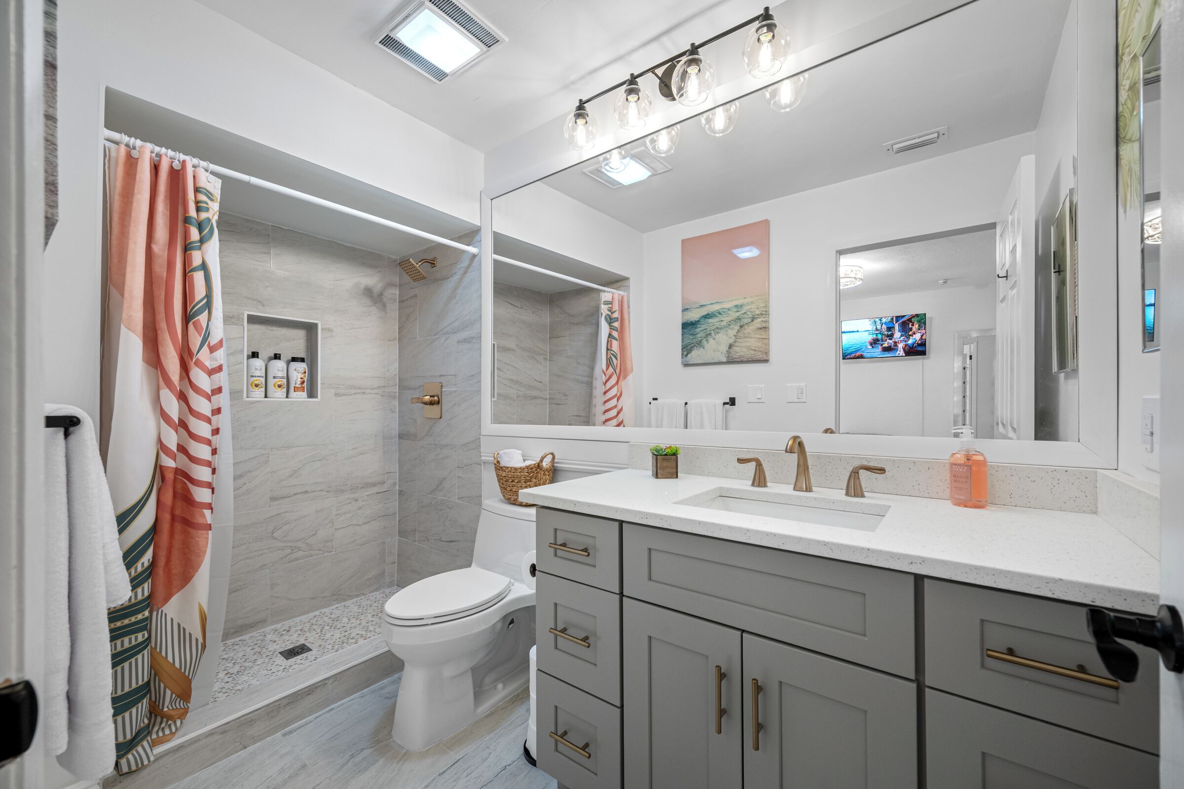 Un baño moderno con ducha, inodoro, tocador y un espejo grande.