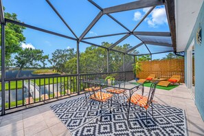 A covered outdoor area with a glass table and chairs, a patterned rug, and a view of a water body and greenery. - Lakefront retreat - Heated Pool - 8 miles to Clearwater beach (Clearwater)