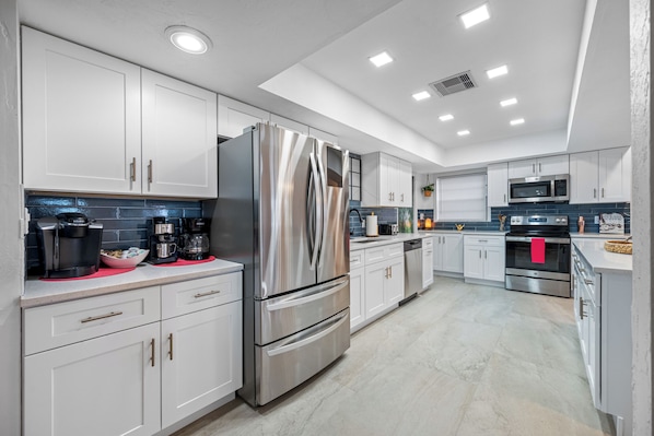 A modern kitchen with stainless steel appliances, white cabinetry, and a tiled backsplash.