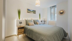 Et soveværelse med seng, sengeborde, lampe, et billede på væggen og et vindue.