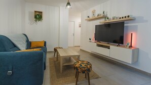 En moderne stue med sofa, sofabord, fjernsyn og reol med pynteting.