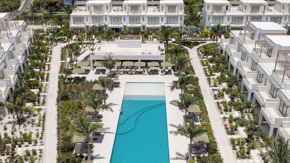Um hotel moderno com piscina central, várias varandas e paisagismo exuberante.