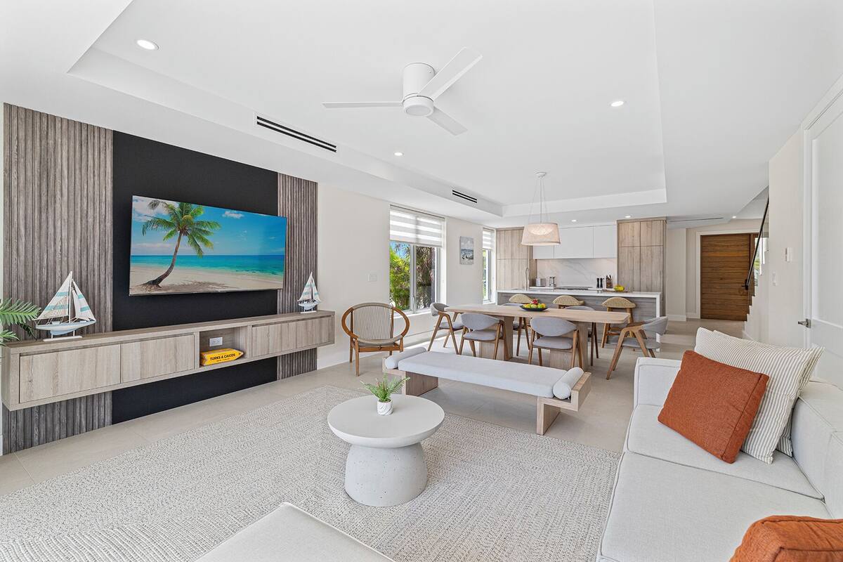 A modern living room with a flat-screen TV, a dining area, and a kitchen.