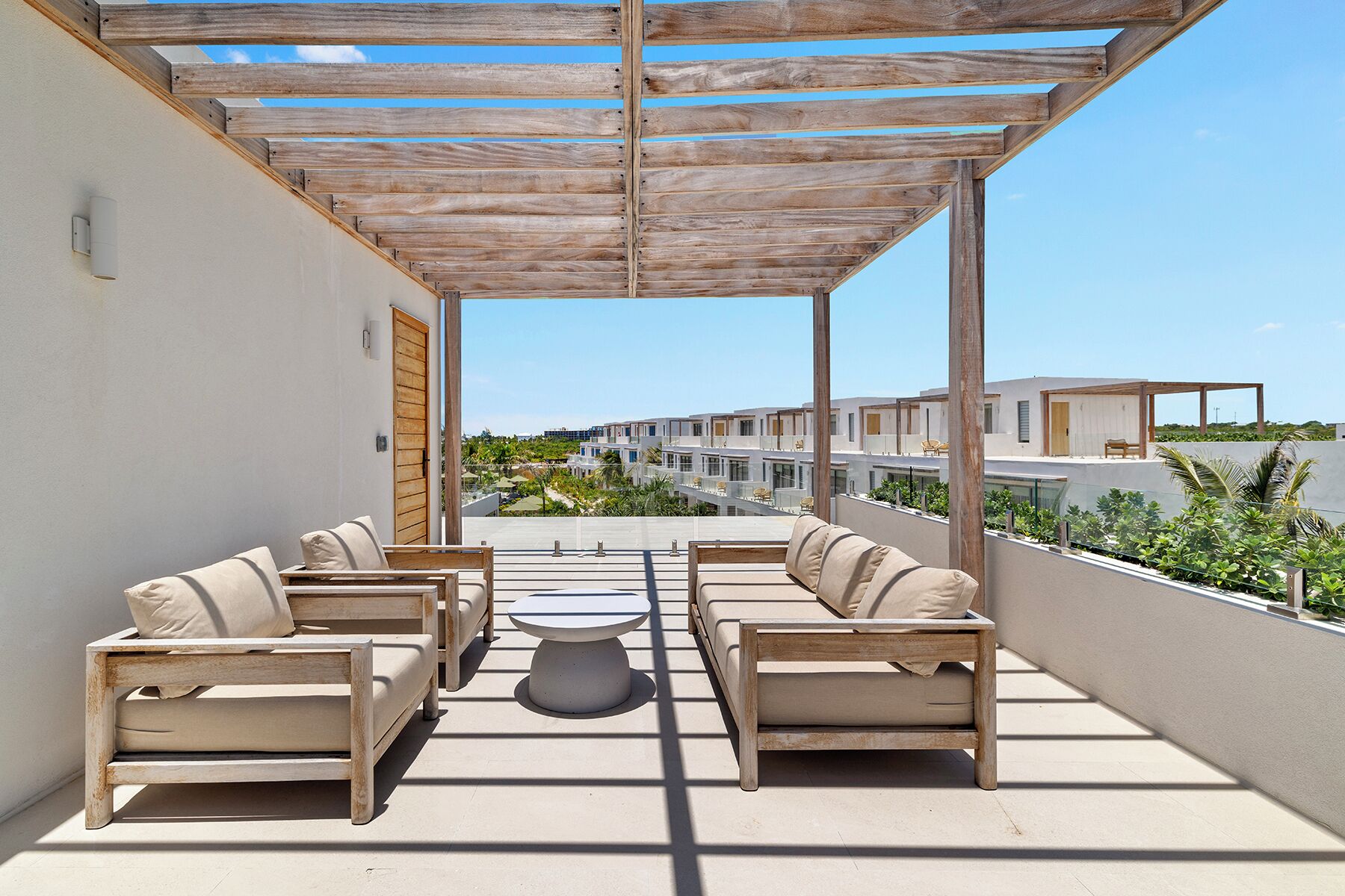 Un espacio exterior techado con mobiliario de madera y vista a un complejo moderno de edificios.
