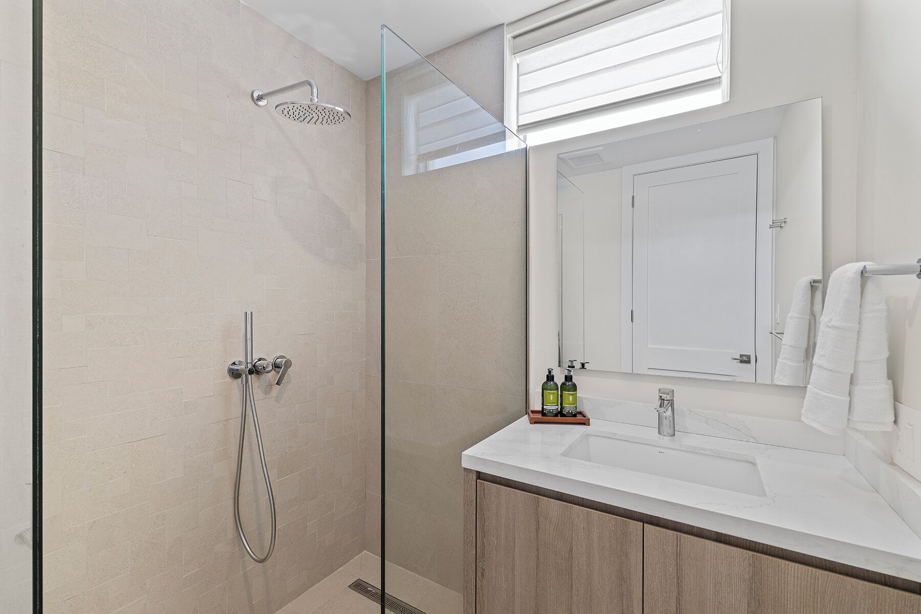 A modern bathroom with a glass shower enclosure, a white sink, and a large mirror above the vanity.