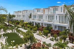 Un hôtel moderne composé de plusieurs bâtiments blancs à étages, doté d’espaces extérieurs aménagés pour se détendre et d’un jardin bien entretenu.