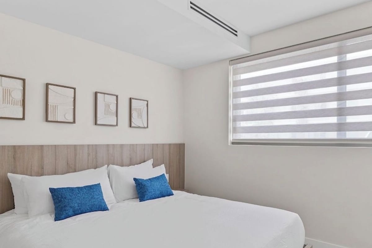 Une chambre moderne avec un grand lit, une tête de lit et une fenêtre avec des stores.