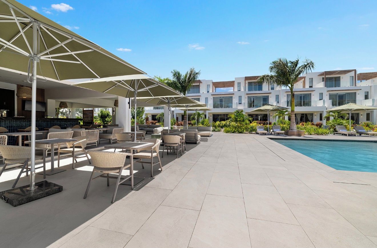 A poolside area with outdoor seating and umbrellas, a pool, and modern buildings in the background.
