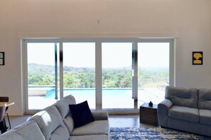 Habitación con sofá, una mesa de centro y vista a una piscina a través de grandes puertas de vidrio.