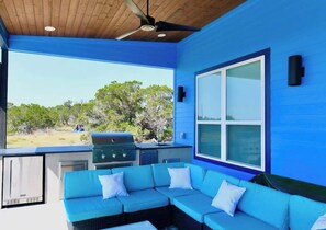 Un espacio exterior techado con una pared azul, un ventanal grande, una parrilla y un sofá azul.