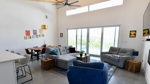 Amplia sala de estar con una mesa de comedor, dos sofás, un sillón azul y un ventanal con vistas.
