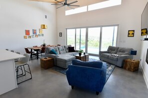 Amplia sala de estar con una mesa de comedor, dos sofás, un sillón azul y un ventanal con vistas.
