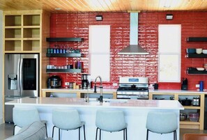 Una cocina moderna con una isla central, electrodomésticos de acero inoxidable y paredes con azulejos rojos.