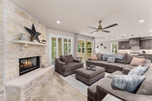 Ein Wohnzimmer mit Kamin aus Stein, grauen Sofas und Deckenventilator.