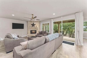 A modern living room with a fireplace, a ceiling fan, and a large sliding glass door leading to a balcony. - Canyon Star | Private Lake Home • Group Retreat (Canyon Lake)