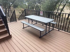 Une terrasse en bois avec une table de pique-nique et des bancs, entourée d’une rambarde en métal noir.