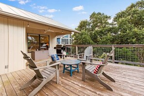 Une terrasse avec des fauteuils Adirondack, une table ronde et un espace barbecue.
