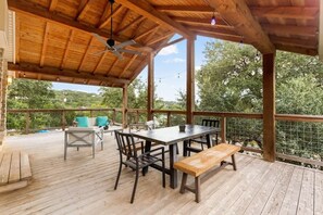 An outdoor wooden deck with a table and chairs, a bench, and a ceiling fan.