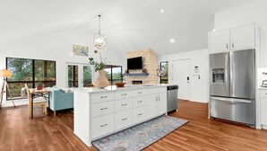 A modern kitchen with a stone fireplace, white cabinetry, and a large stainless steel refrigerator.